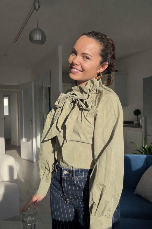 Blouse vert sauge élégante à col lavallière portée avec un jean